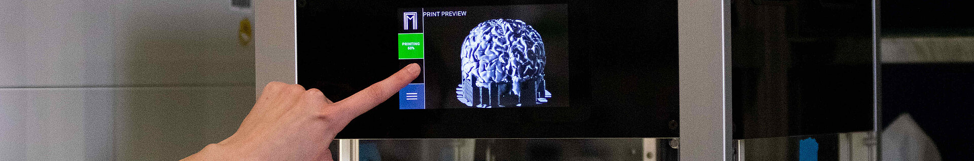 Eine Hand am Display eines 3D-Druckers im Labor.