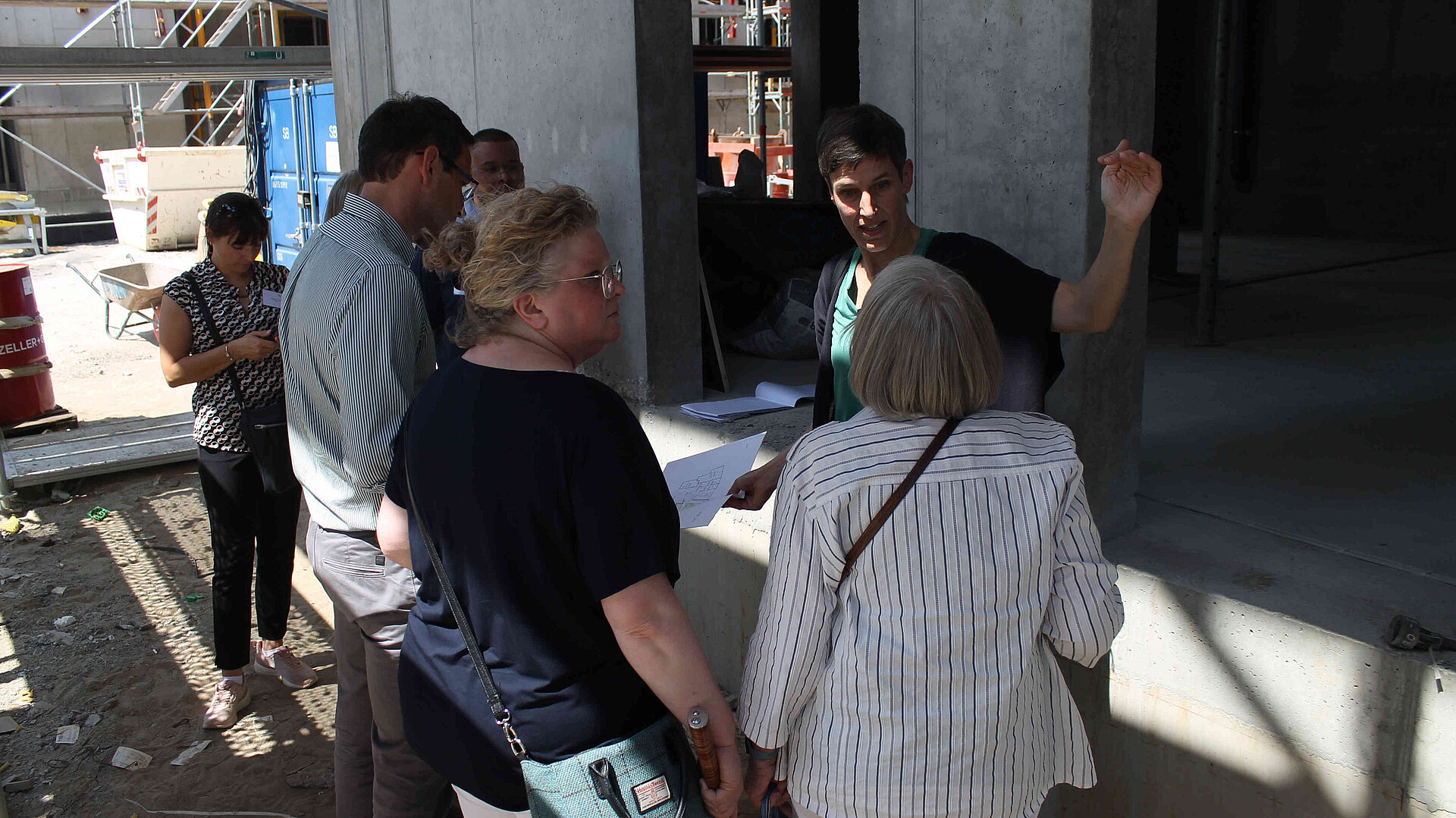 Eine Frau erklärt Menschen etwas auf einer Baustelle.