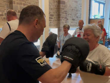 Ein Mann hält Boxpratzen. Eine Frau boxt dagegen.