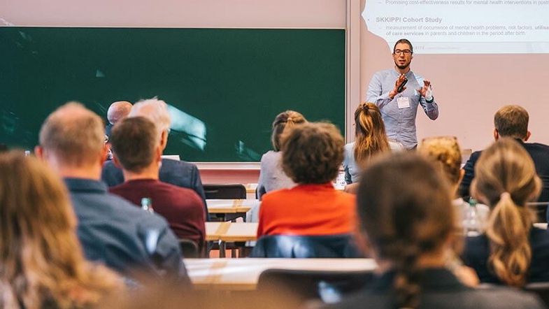Ein Mensch spricht in einem Saal vor einem Publikum.
