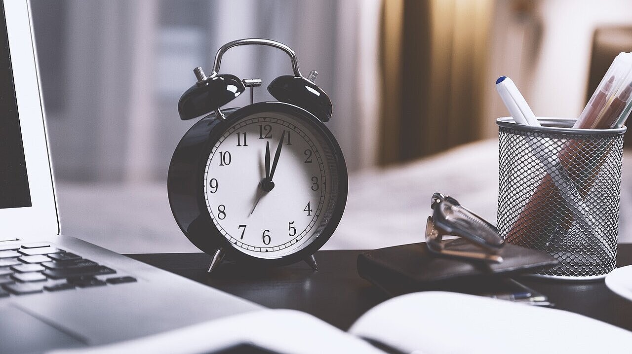 Ein Wecker neben einem Laptop auf einem Tisch.