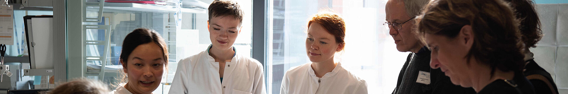 Eine Wissenschaftlerin erklärt Menschen in einem Labor eine Abbildung, die sie in Händen hält.