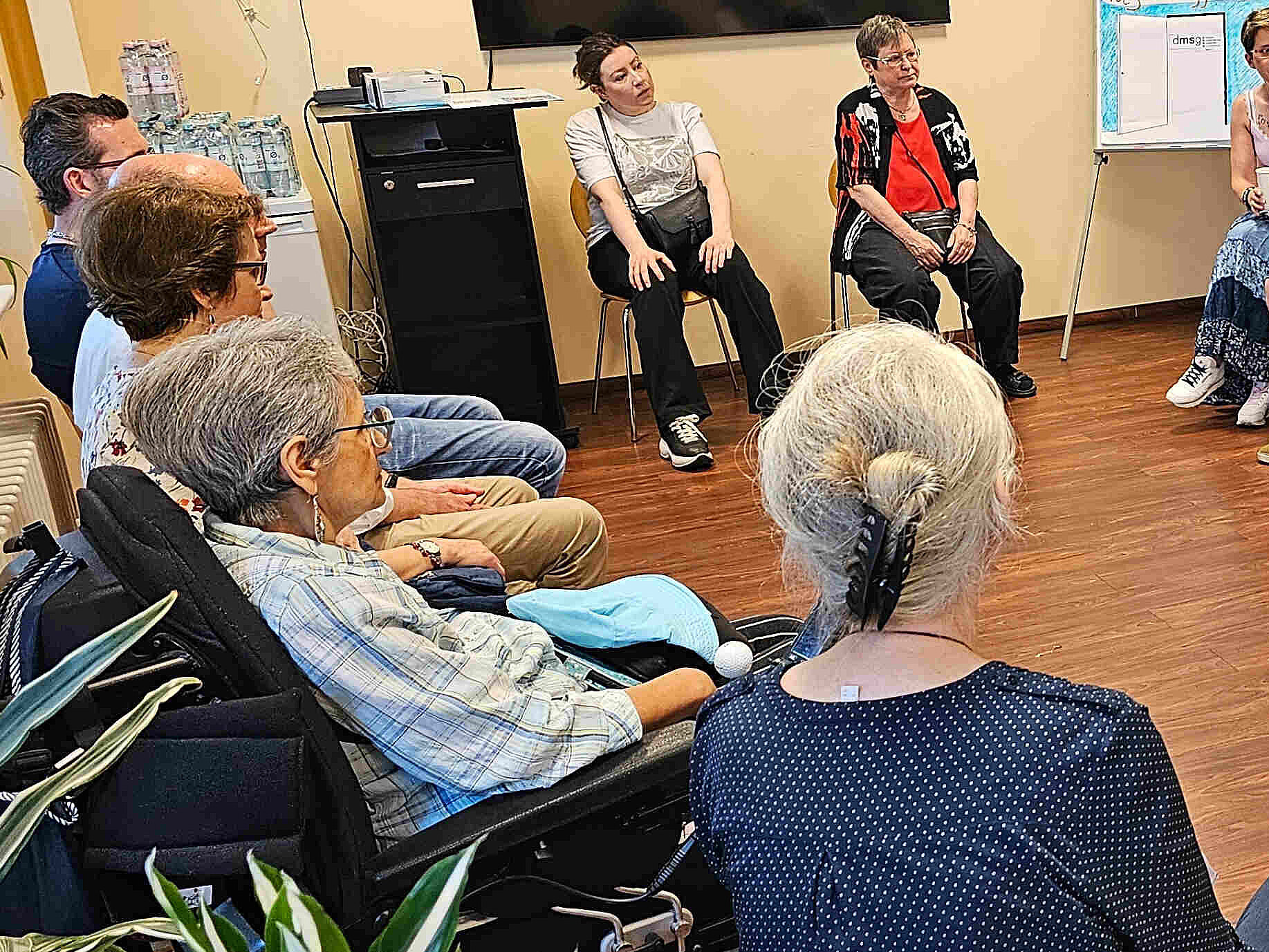 Menschen auf Stühlen in einem Raum.