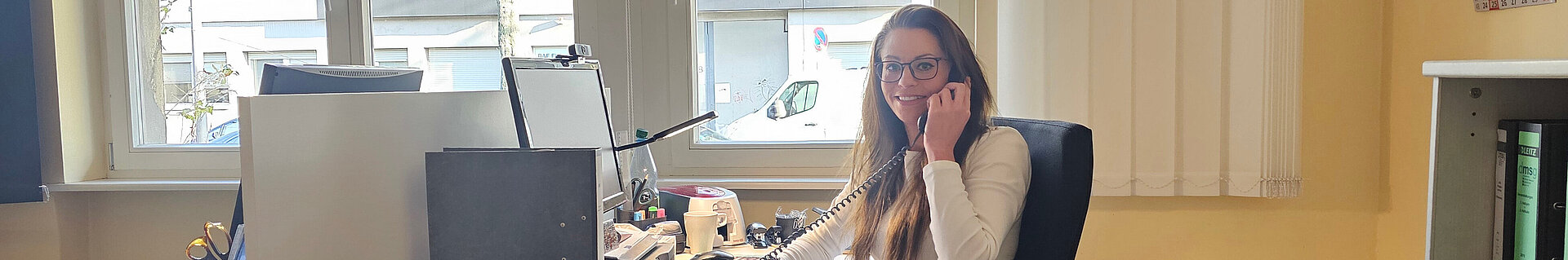 Eine Frau am Schreibtisch mit einem Telefonhörer in der Hand.