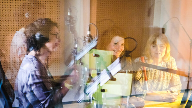 Drei Frauen sitzen in einem Tonstudio vor Mikrofonen.