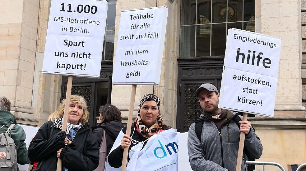 Drei Menschen mit bedruckten Demo-Schildern.