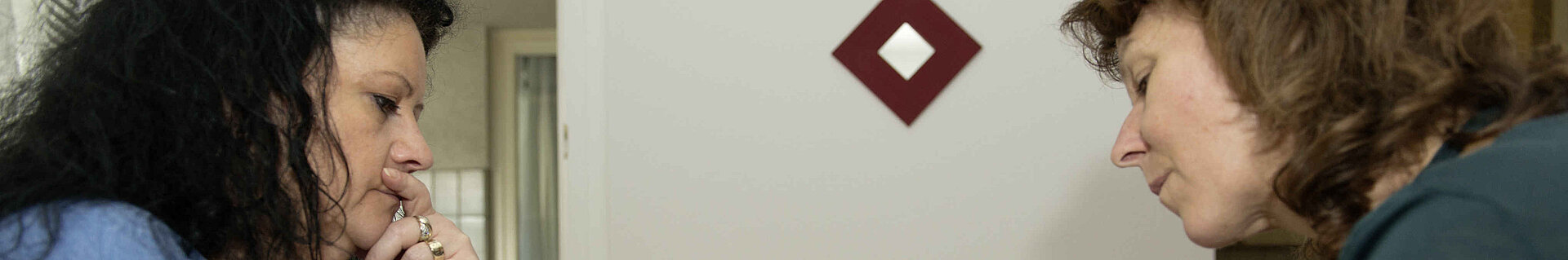 Zwei Frauen sitzen sich an einem Tisch in einer Wohnung gegenüber und reden.