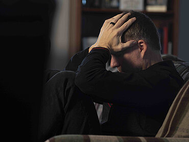 Depression Ein Mann mit gesenktem Kopf und Händen an der Stirn in einem Stuhl.