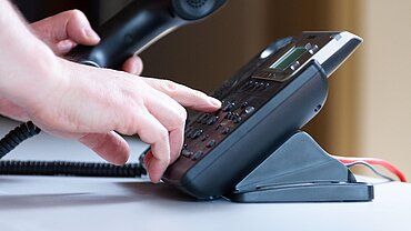 Eine Hand an einem Bürotelefon.
