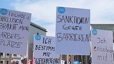 Plakate mit Forderungen zur Gleichstellung von Menschen mit Behinderungen auf einer Demonstration.
