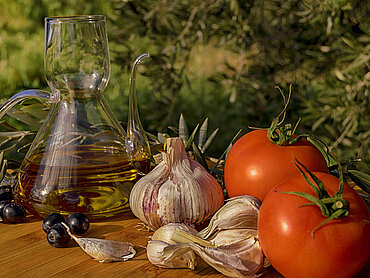 Essen Knoblauch, Tomaten und eine Karaffe mit Olivenöl auf einem Tisch.