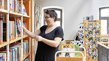 Eine Frau sortiert Bücher in die Regale einer Bibliothek ein.