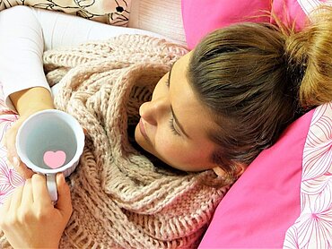 Eine Frau mit einer Tasse im Bett.