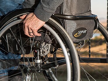 Mann mit den Händen an den Rädern seines Rollstuhls. 
