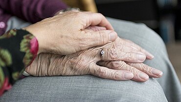 Eine Hand liegt auf zwei Händen einer alten Person.