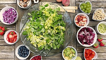 Schüsseln mit Gemüse, Obst und Nüssen auf einem Tisch.