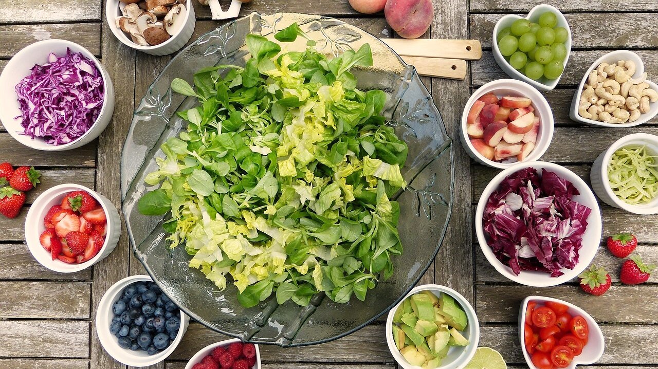 Schüsseln mit Gemüse, Obst und Nüssen auf einem Tisch.