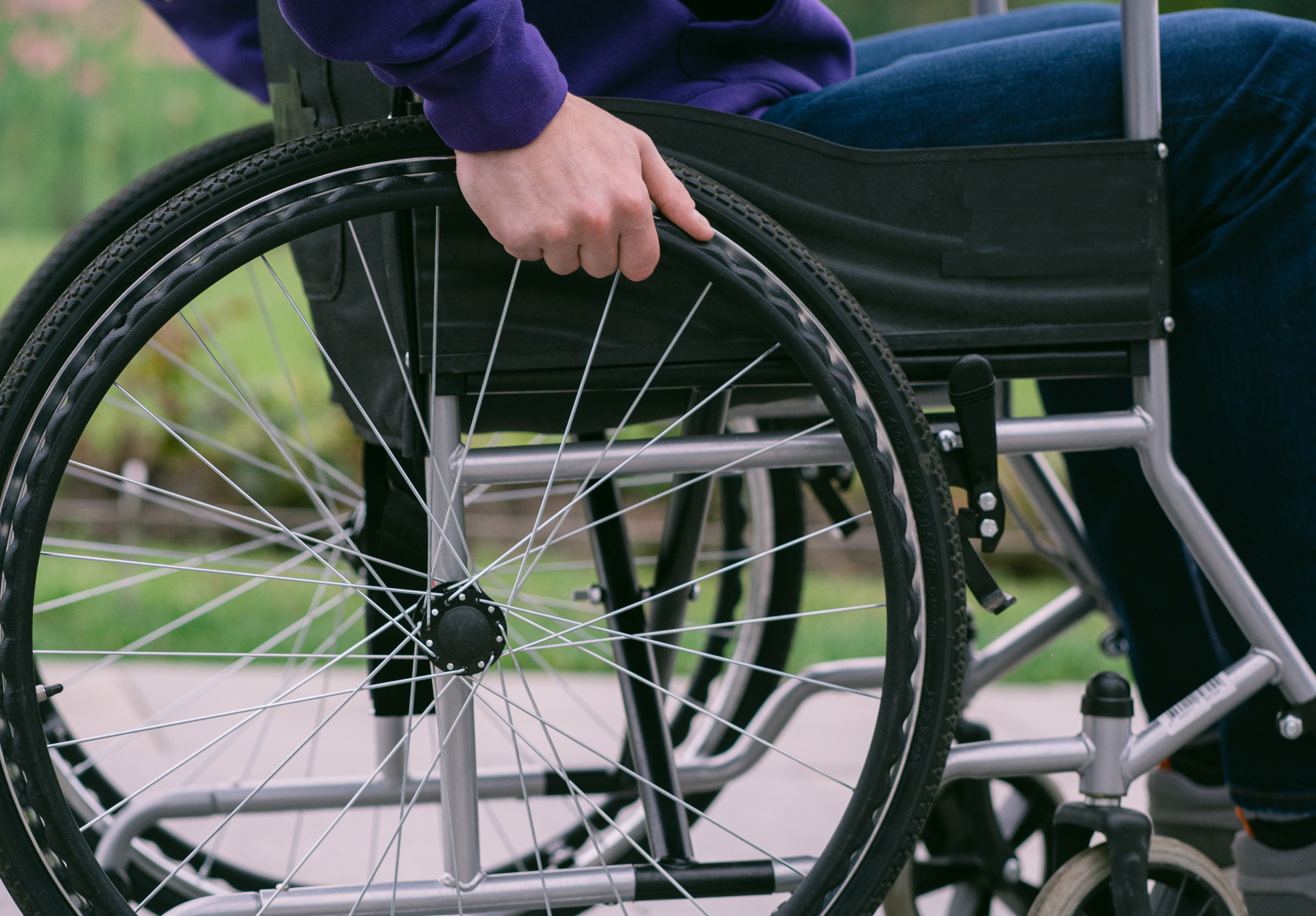 Auf dem Bild sieht man das Rad eines Rollstuhl und die Beine der Person, die darin sitzt.